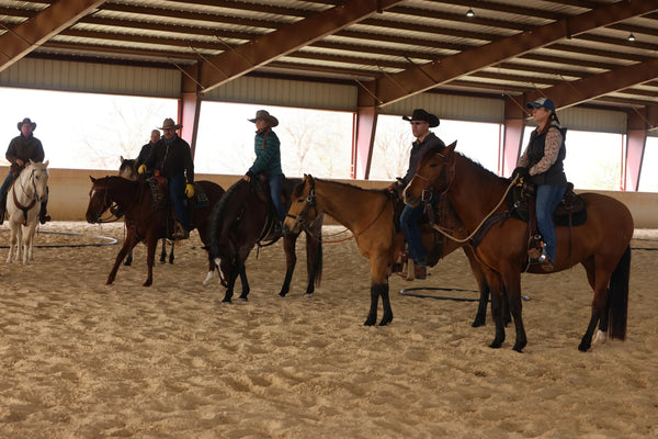 Group of people riding horses in an indoor arena.