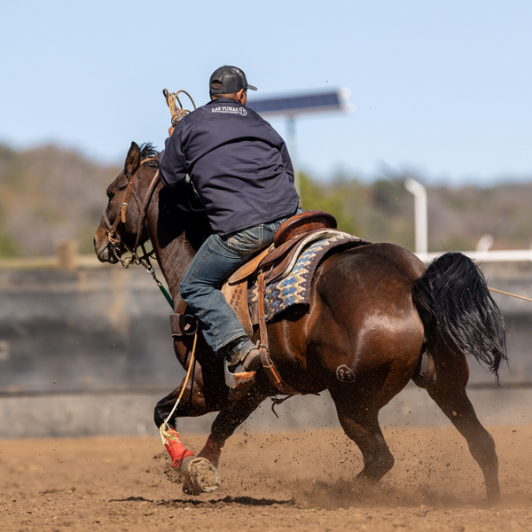 Person riding a horse on a dirt track with a clear sky in the background