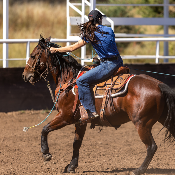 Woman riding a brown horse in an outdoor setting with a white fence in the background